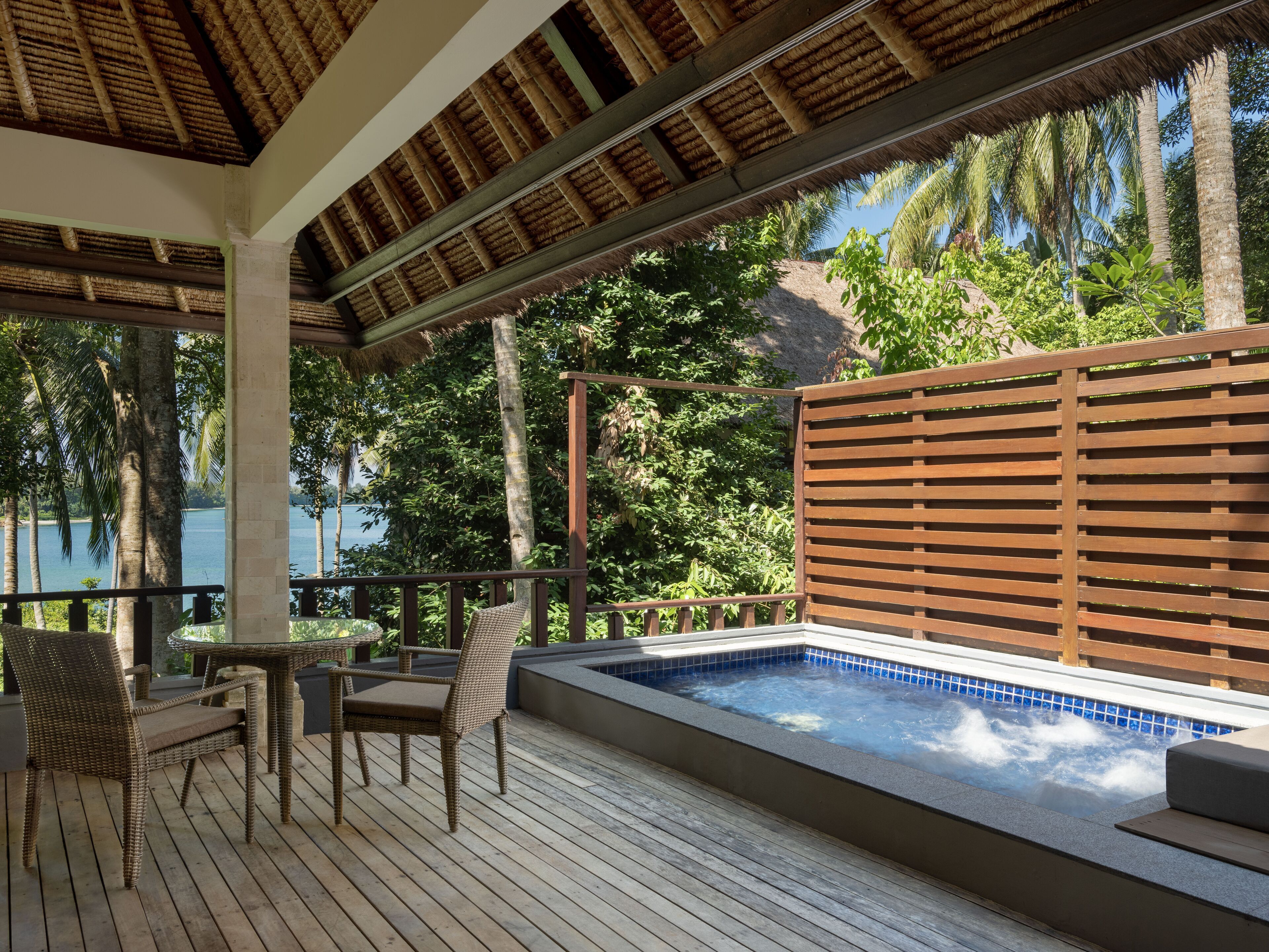 A wooden deck with a hot tub, wicker chairs, and a view of a body of water.