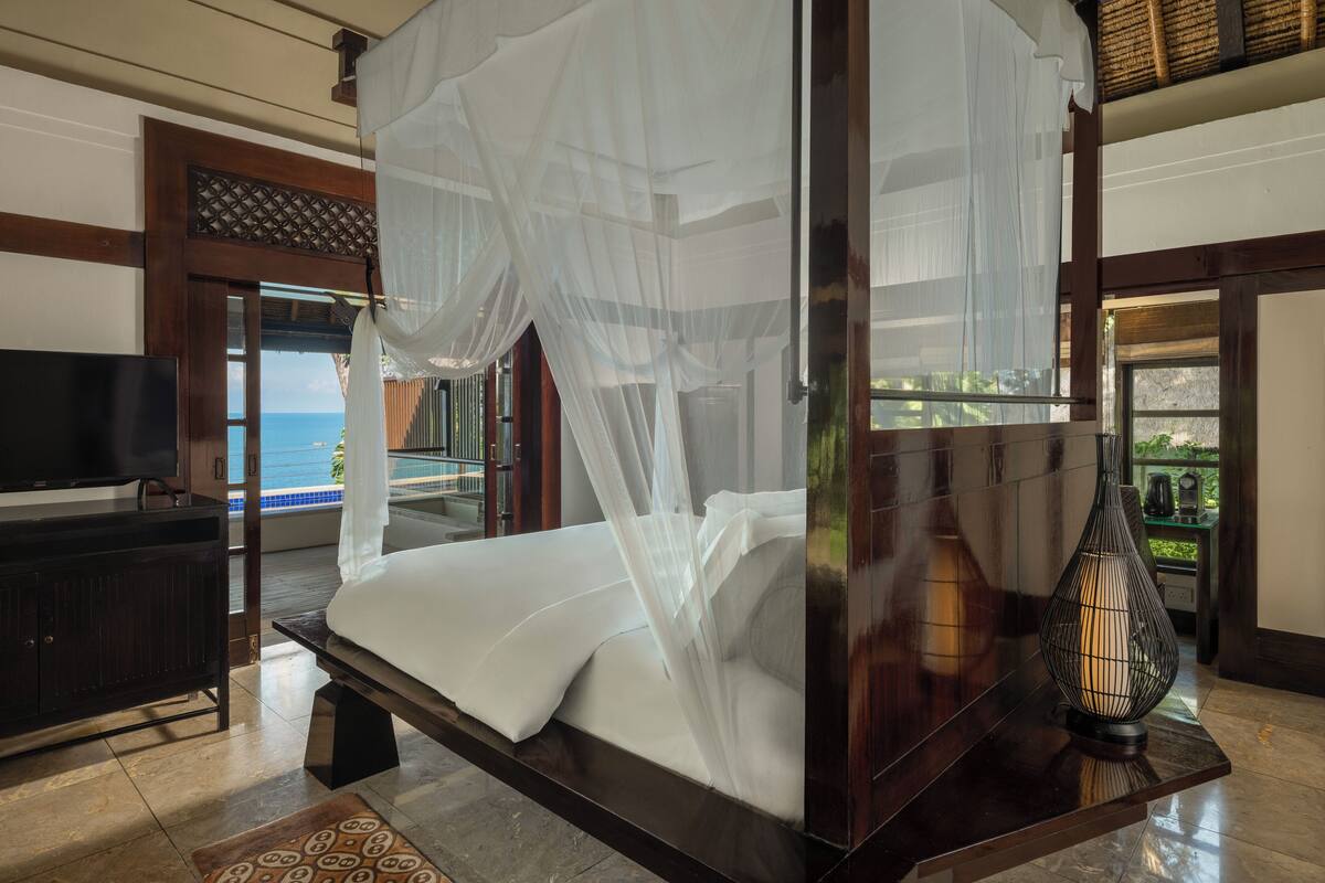 A four-poster bed with a canopy, a television on a stand, and a view of the sea through a glass door.