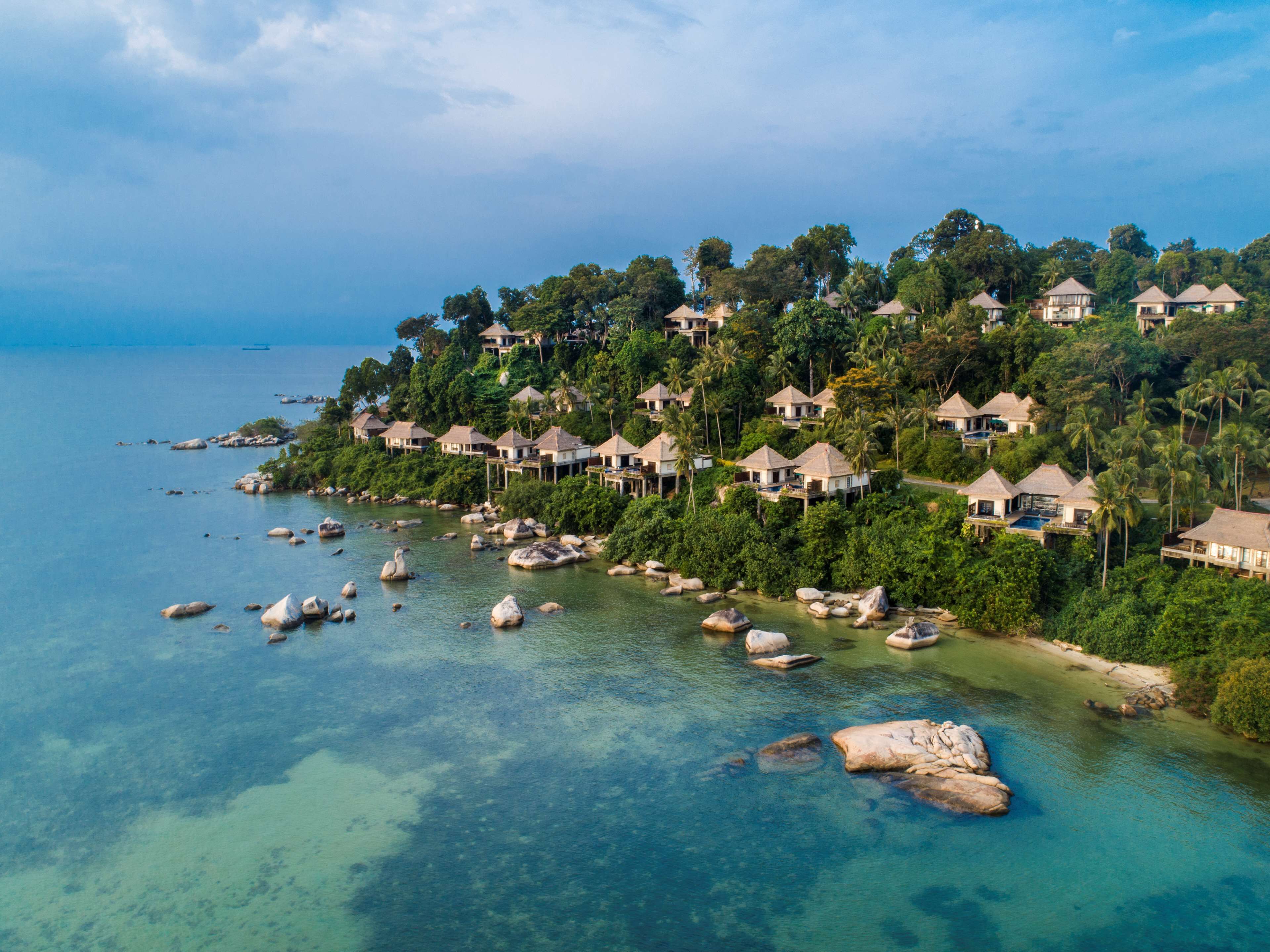 Un resort costero con varias edificaciones tipo bungalow, aguas turquesas cristalinas y afloramientos rocosos.