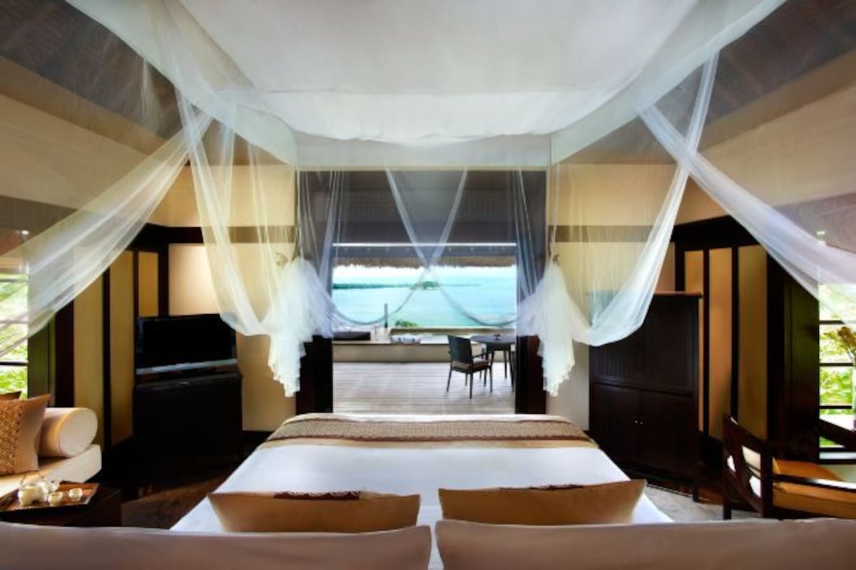 A hotel room with a bed, a TV, a dining area, and a view of the sea.