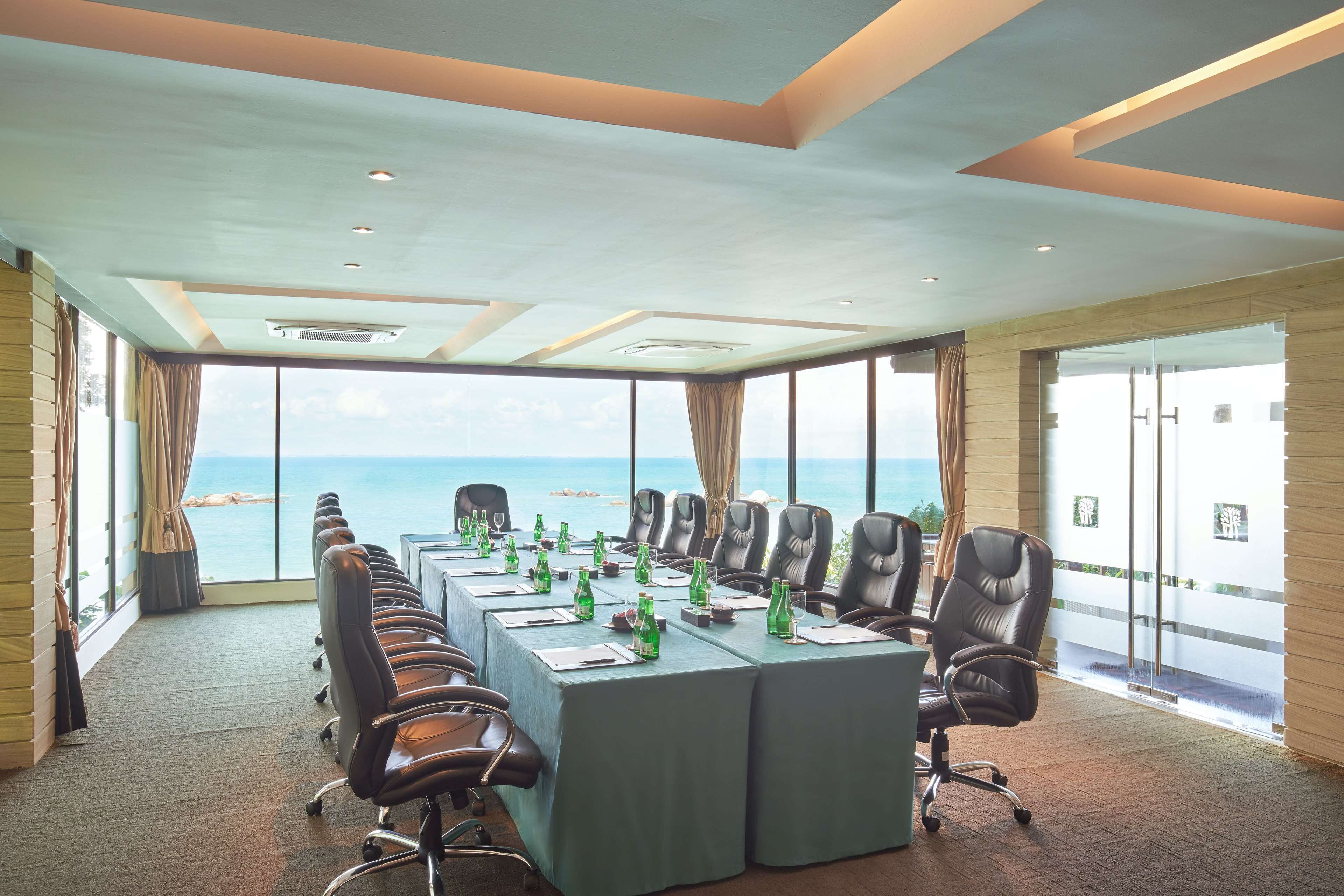 A conference room with a long table, chairs, and a view of the sea.