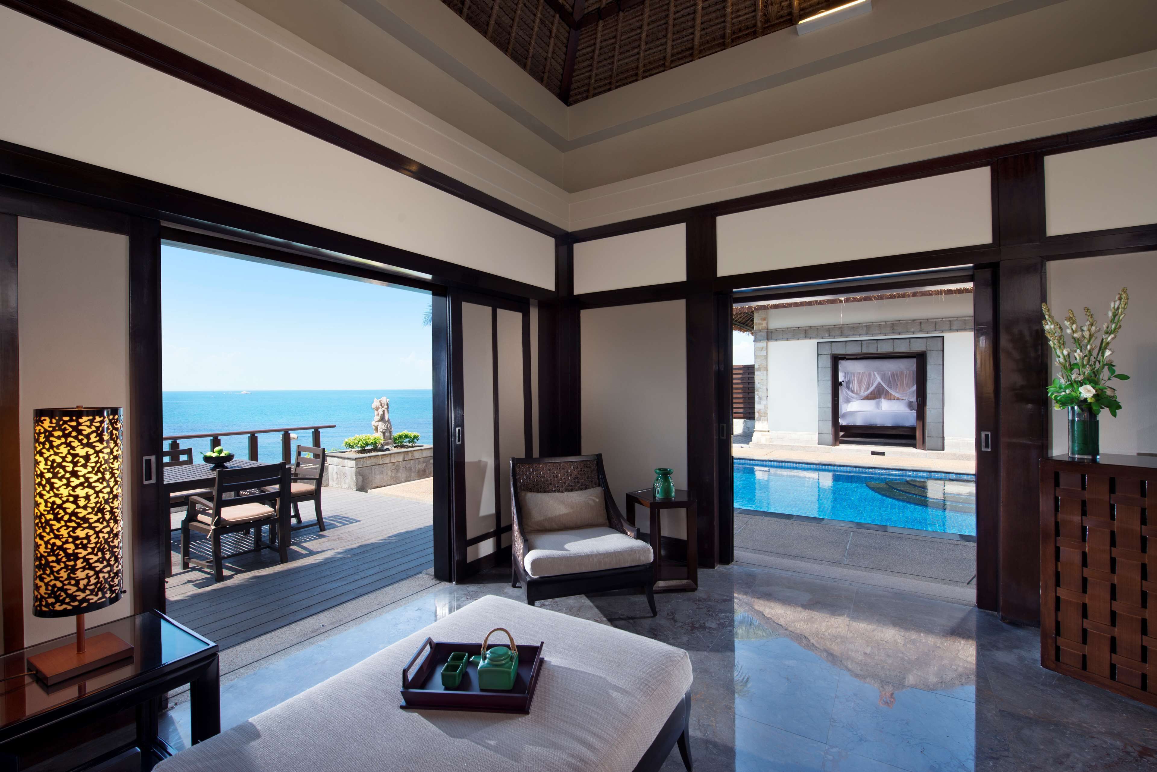 Amplia habitación con un gran ventanal con vistas a una piscina y al mar.