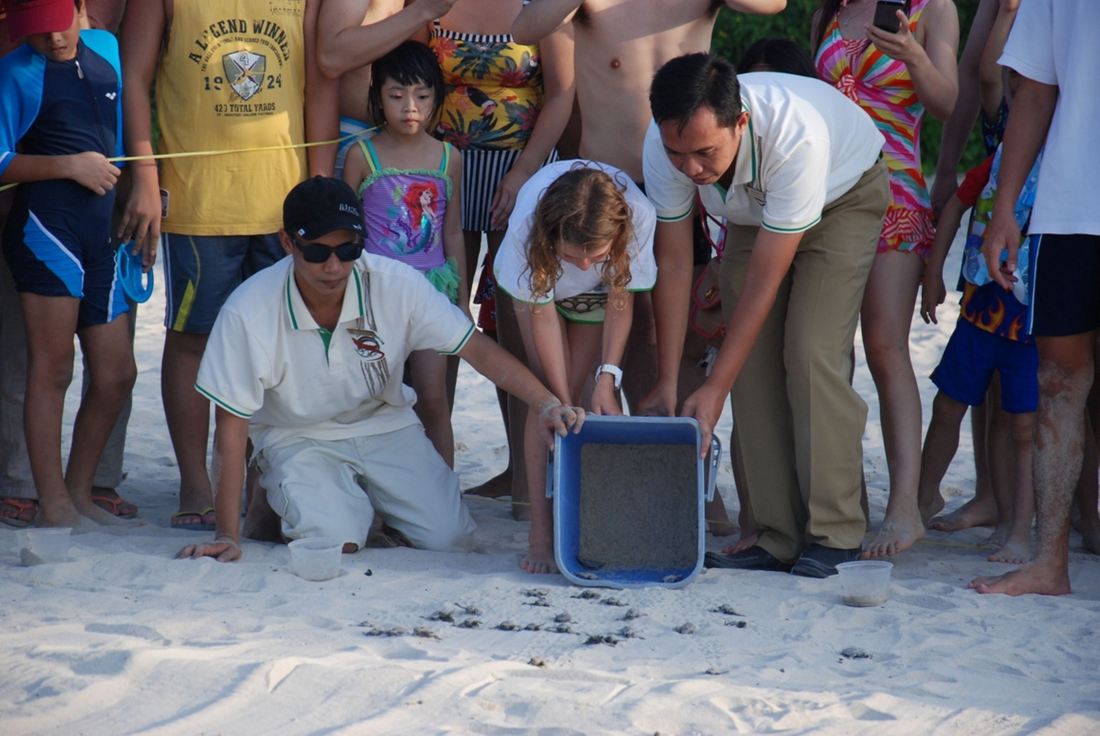 A group of people on a sandy beach, some holding a blue container.