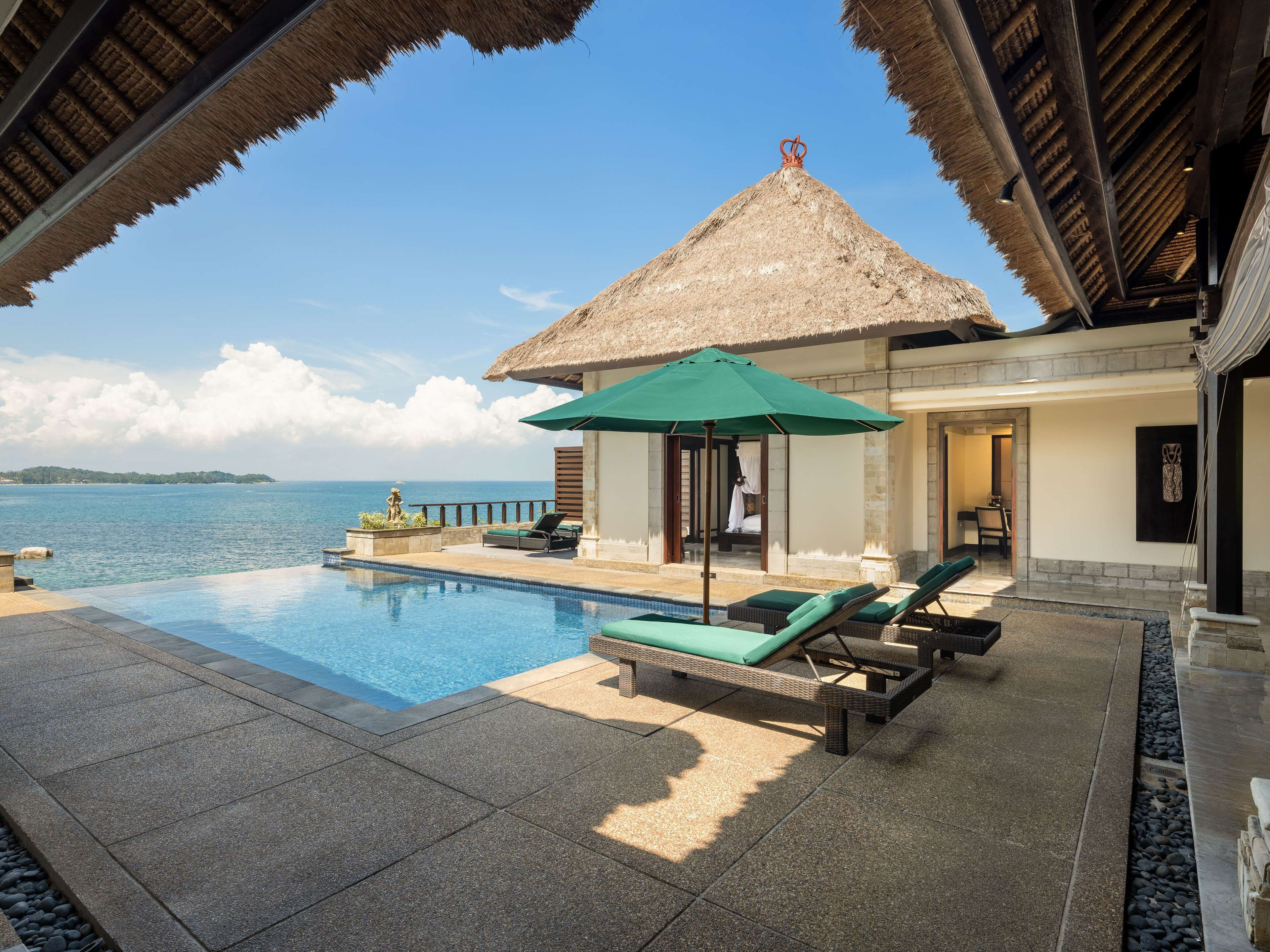 Ein Poolbereich mit Liegestühlen, einer strohgedeckten Struktur und Blick aufs Meer.