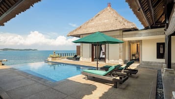 Ein Poolbereich mit Liegestühlen, einer strohgedeckten Struktur und Blick aufs Meer.