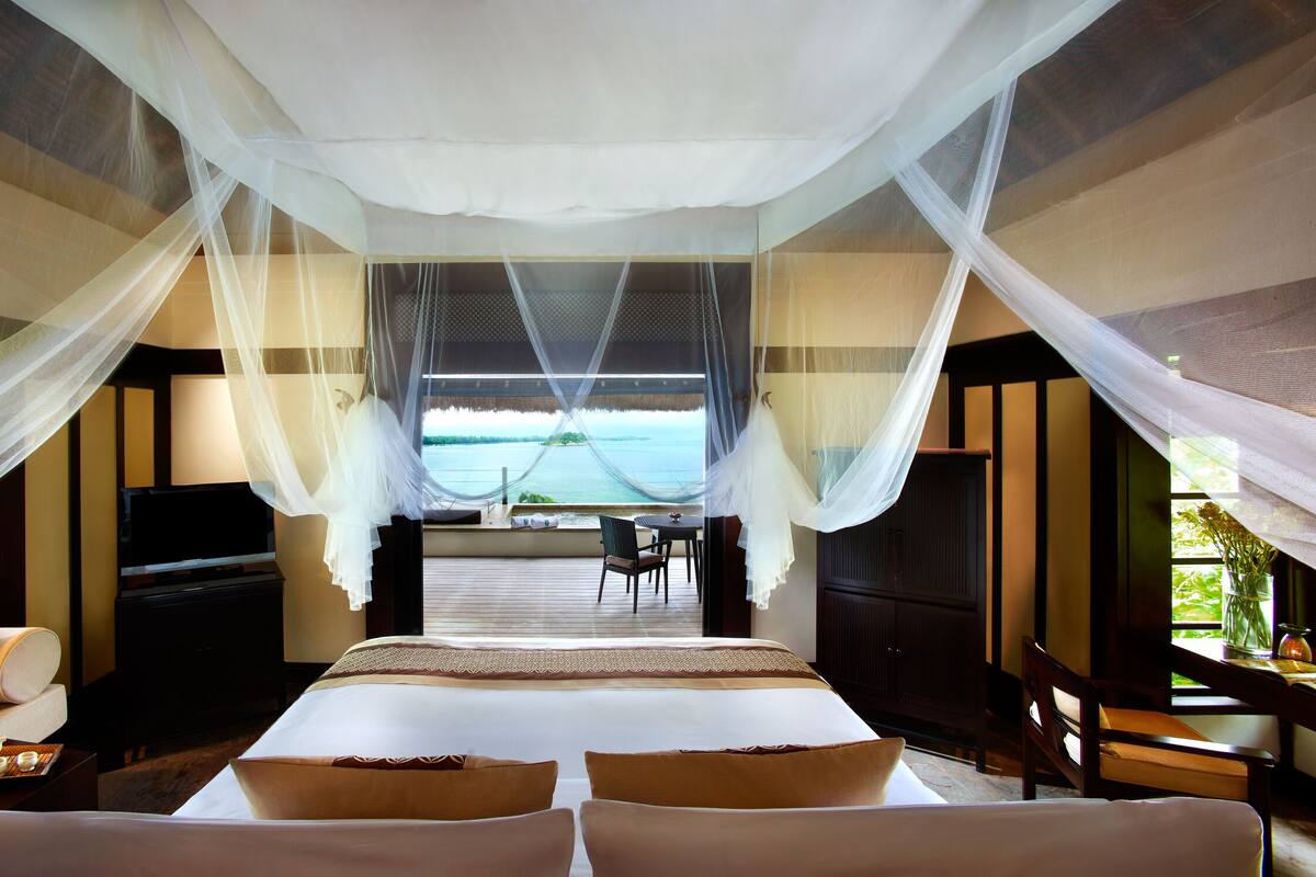 A bedroom with a bed, a TV, and a view of the sea.