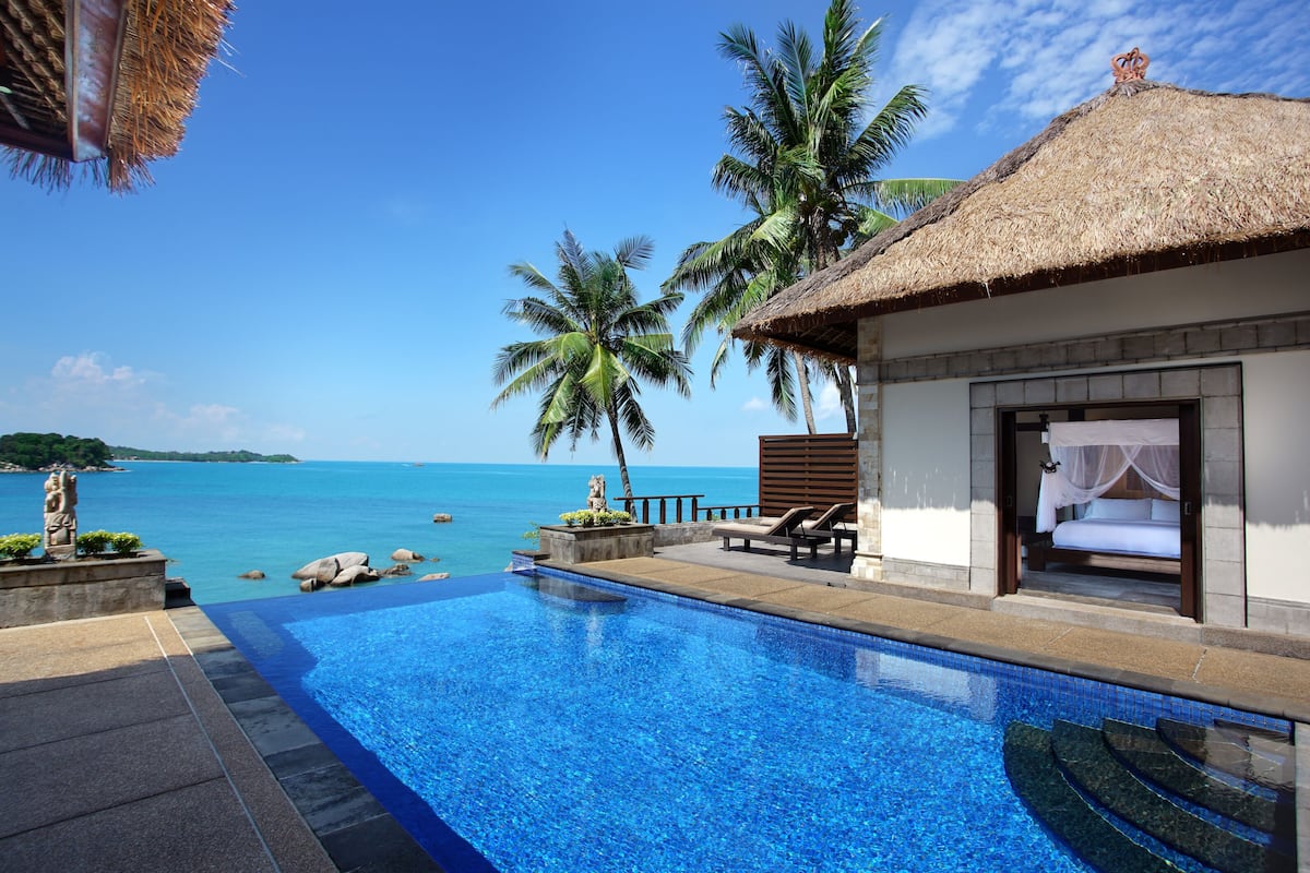 A swimming pool with a view of the ocean, a thatched-roof building, and a statue.