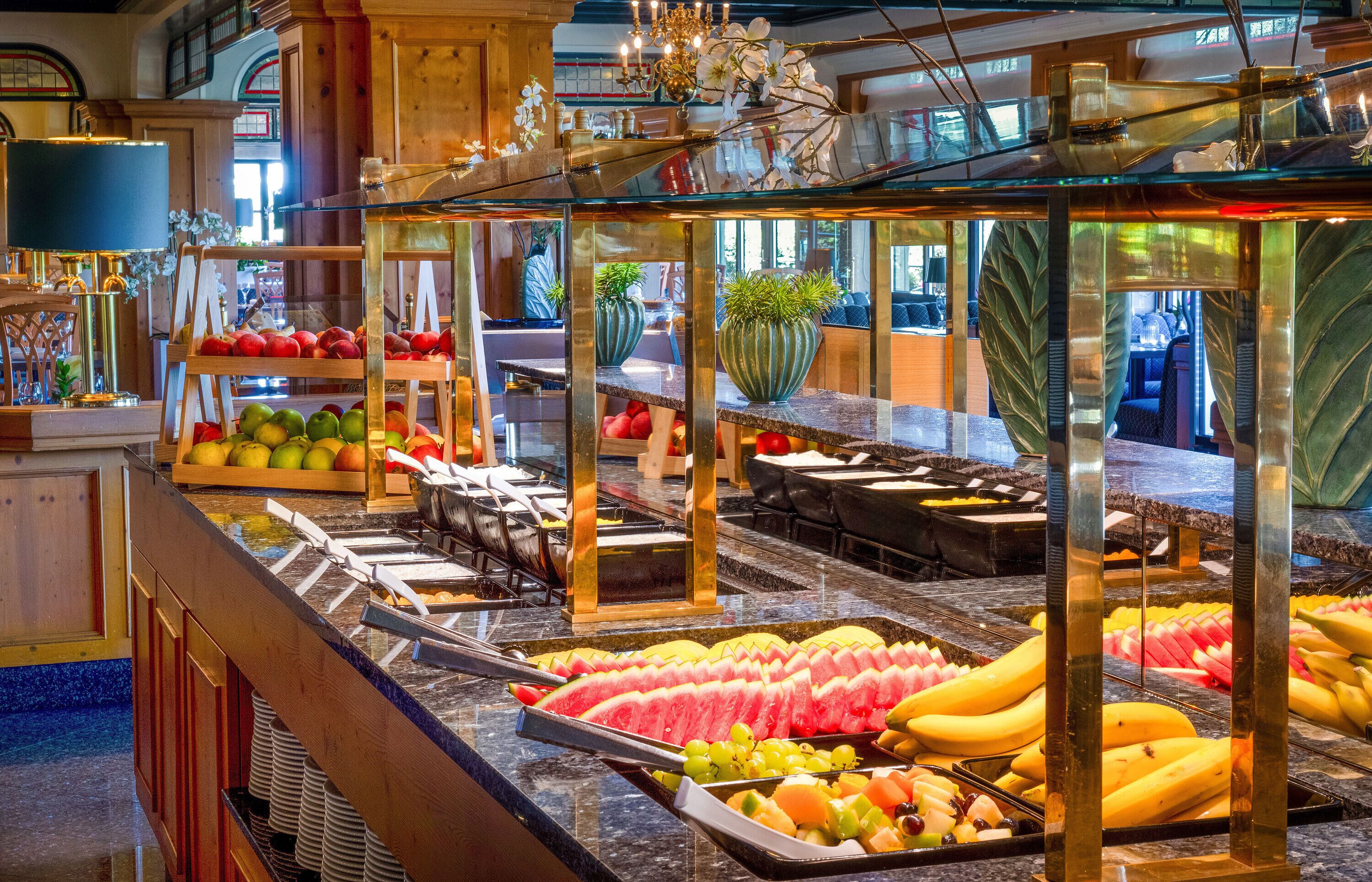 A buffet area with various fruits and vegetables, including watermelon, bananas, and apples.