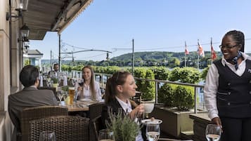 Una terraza con mesas al aire libre, un camarero y vistas al paisaje.