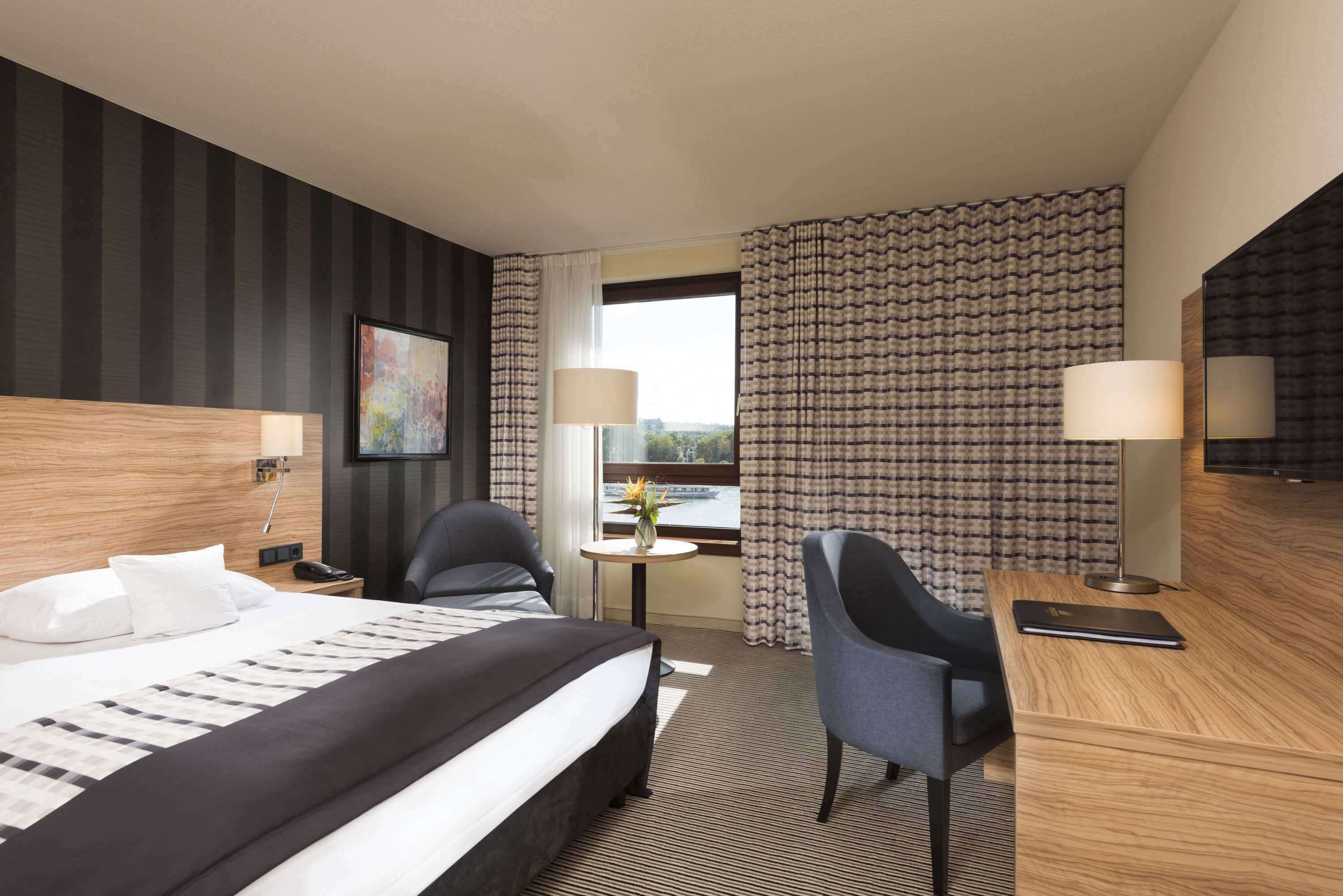 A hotel room with a large bed, two chairs, a desk, and a window with curtains.