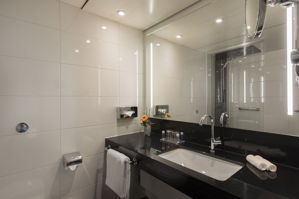 Un baño moderno con lavamanos de superficie negra, un espejo grande y un box de ducha de vidrio.