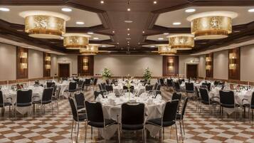 Une vaste salle de banquet avec des tables rondes dressées pour le repas, dotée d’un sol à carreaux et de lustres modernes.