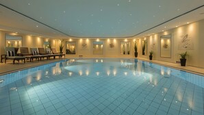 A large indoor swimming pool with a tiled floor, surrounded by lounge chairs and potted plants. - Maritim Hotel Königswinter (Königswinter)