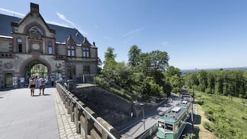 A historic building with a large arched entrance, a green tram on tracks, and a stone wall with a metal railing.