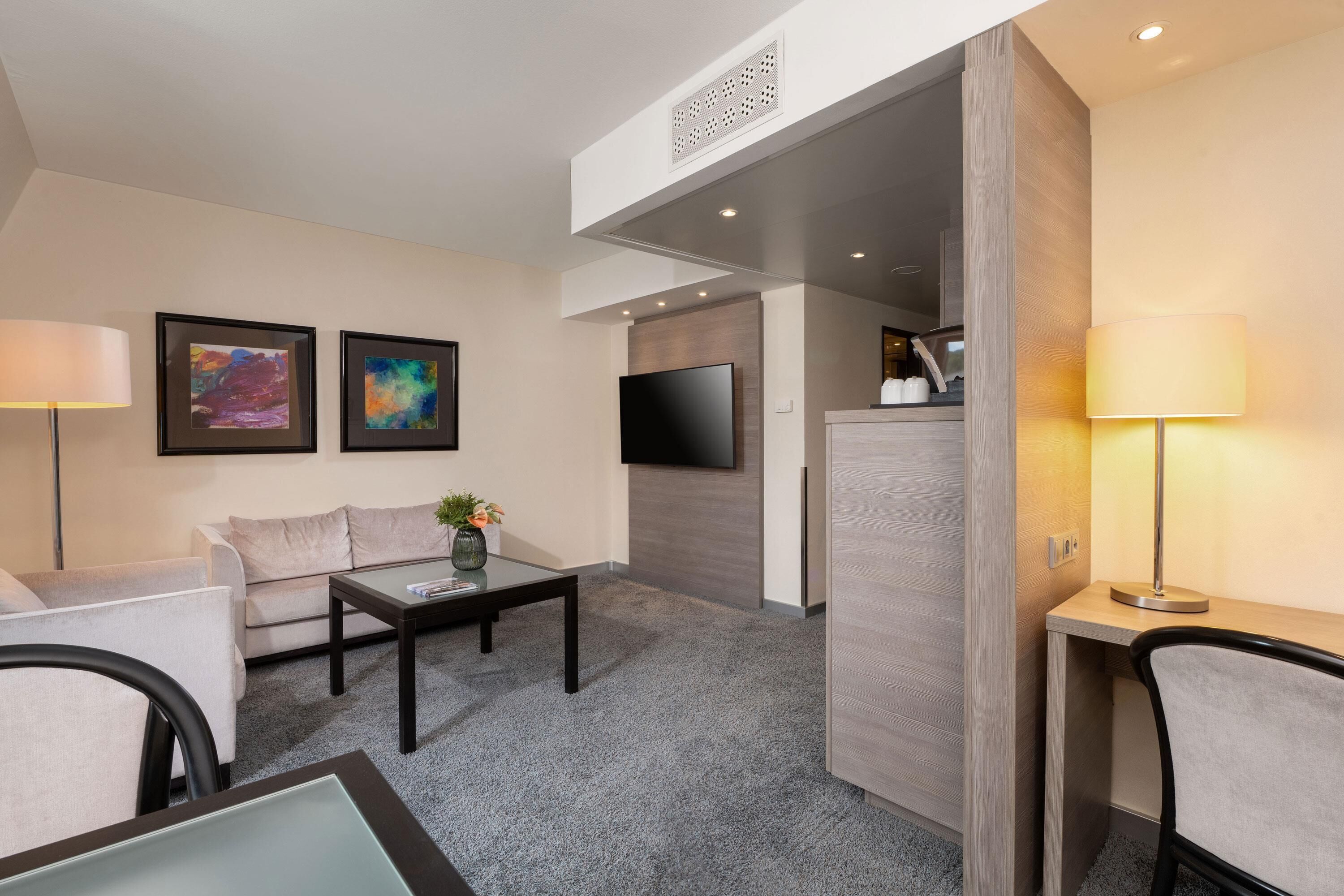 Una habitación de hotel moderna con sofá, una mesa de centro, televisión y un espacio de trabajo.