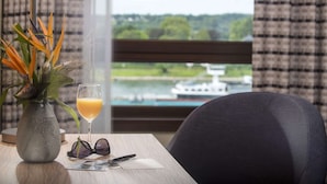 A table with a vase of flowers, a glass of orange juice, and a pair of glasses. A chair is positioned in front of the table. - Maritim Hotel Königswinter (Königswinter)