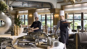 A dining area with buffet setup, including silverware and dishes, and a view of the outdoors. - Maritim Hotel Königswinter (Königswinter)