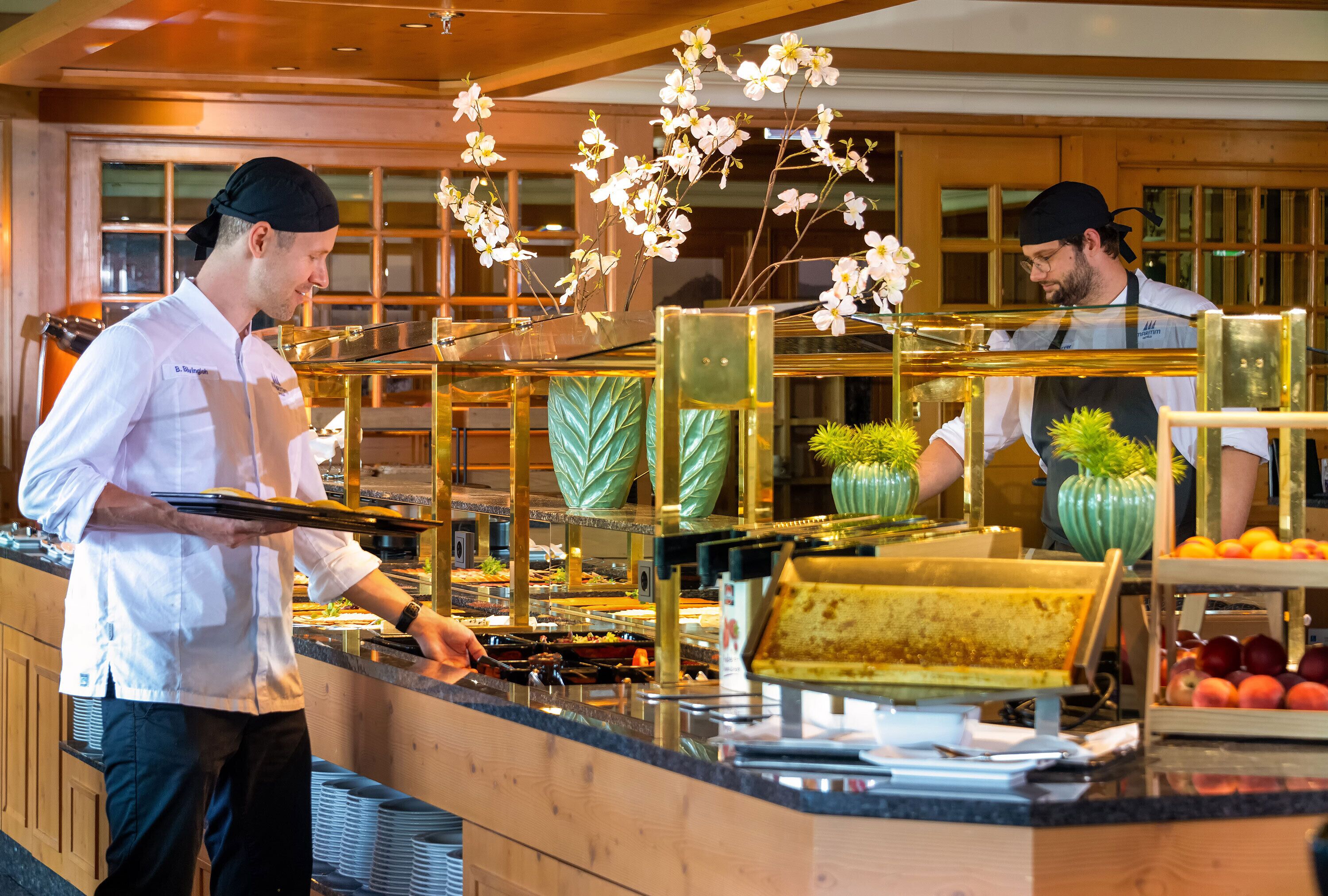 A buffet setup with multiple food stations, a counter with a glass display, and decorative elements like flowers.