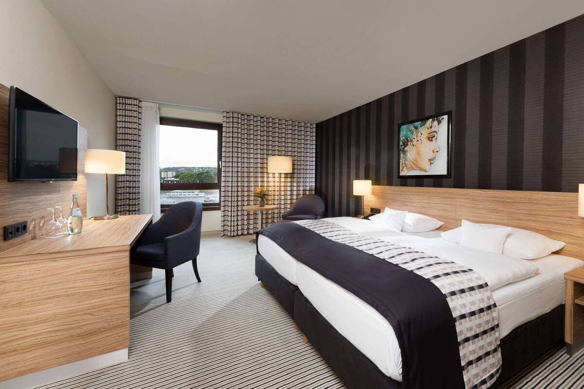 Ein Hotelzimmer mit Bett, Schreibtisch, Stuhl, Lampen und einem Fernseher.