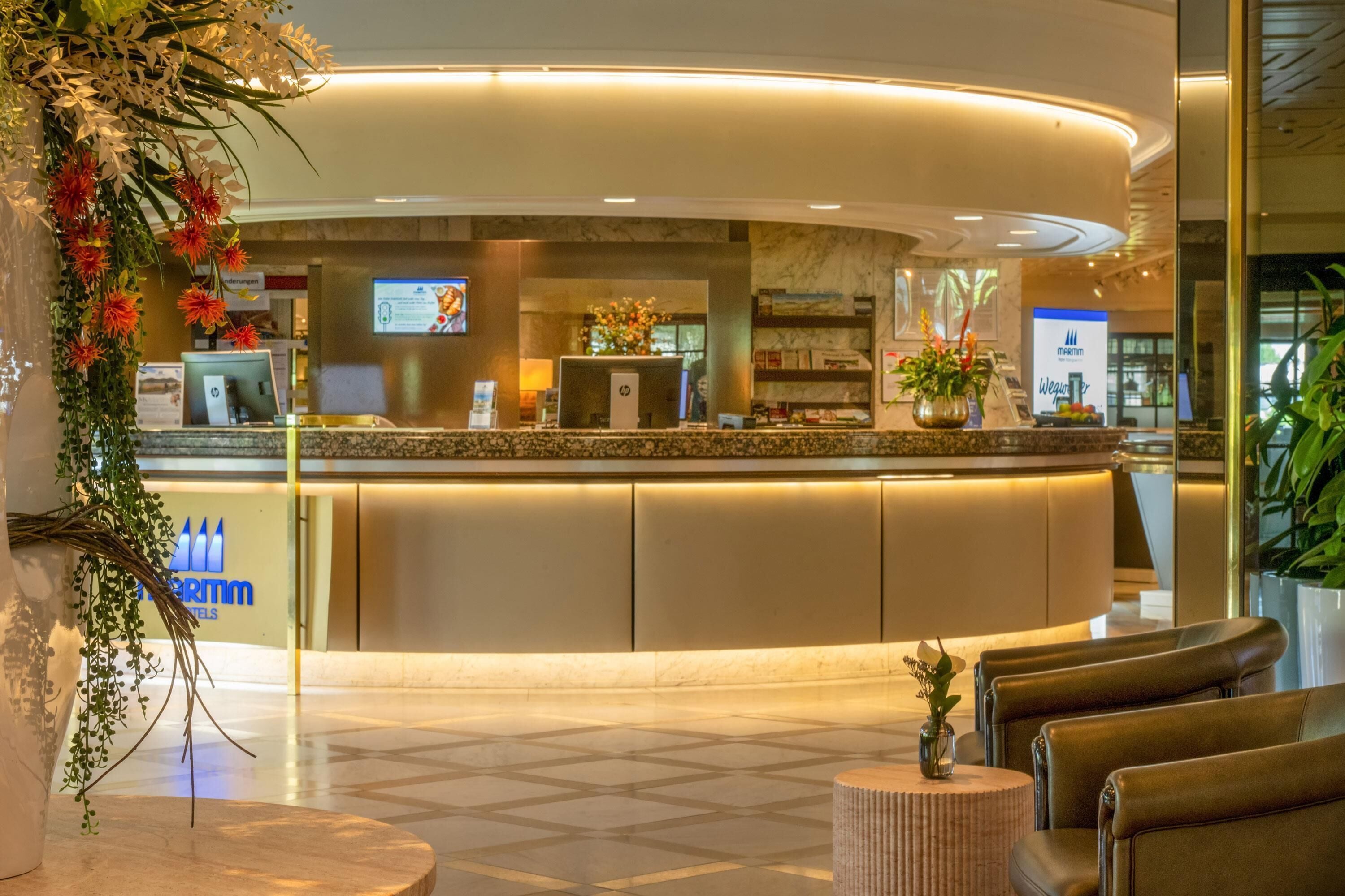 Ein Hotel-Rezeptionsbereich mit einer gebogenen Theke, Sitzgelegenheiten und einer großen Pflanze.