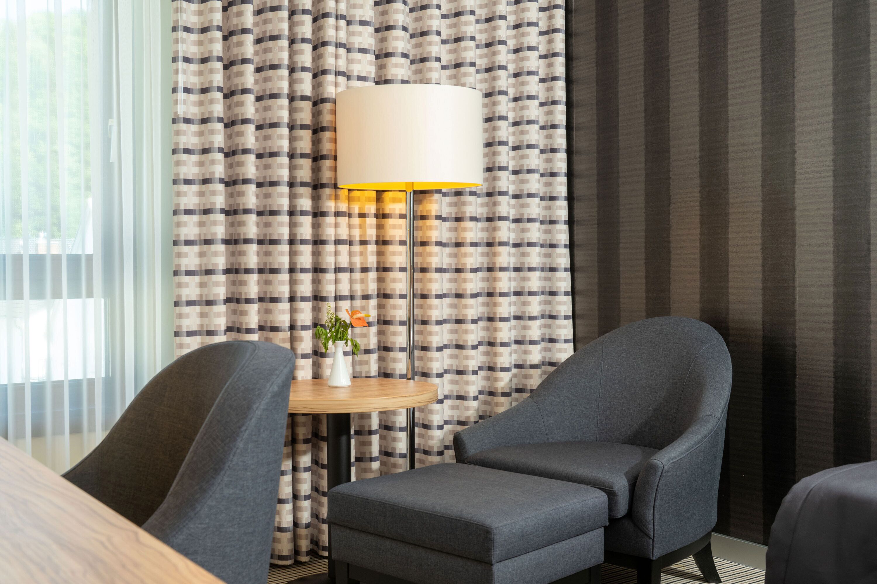 A hotel room with a checkered curtain, a round table with a vase, and two armchairs.
