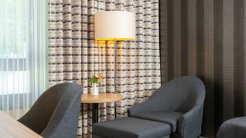A hotel room with a checkered curtain, a round table with a vase, and two armchairs.
