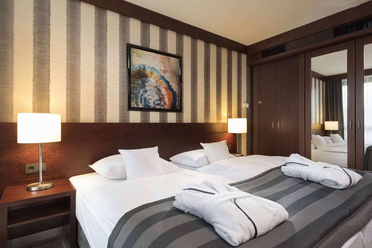Ein Hotelzimmer mit zwei Betten, gestreifter Bettwäsche, einem großen Gemälde an der Wand und einem Kleiderschrank.