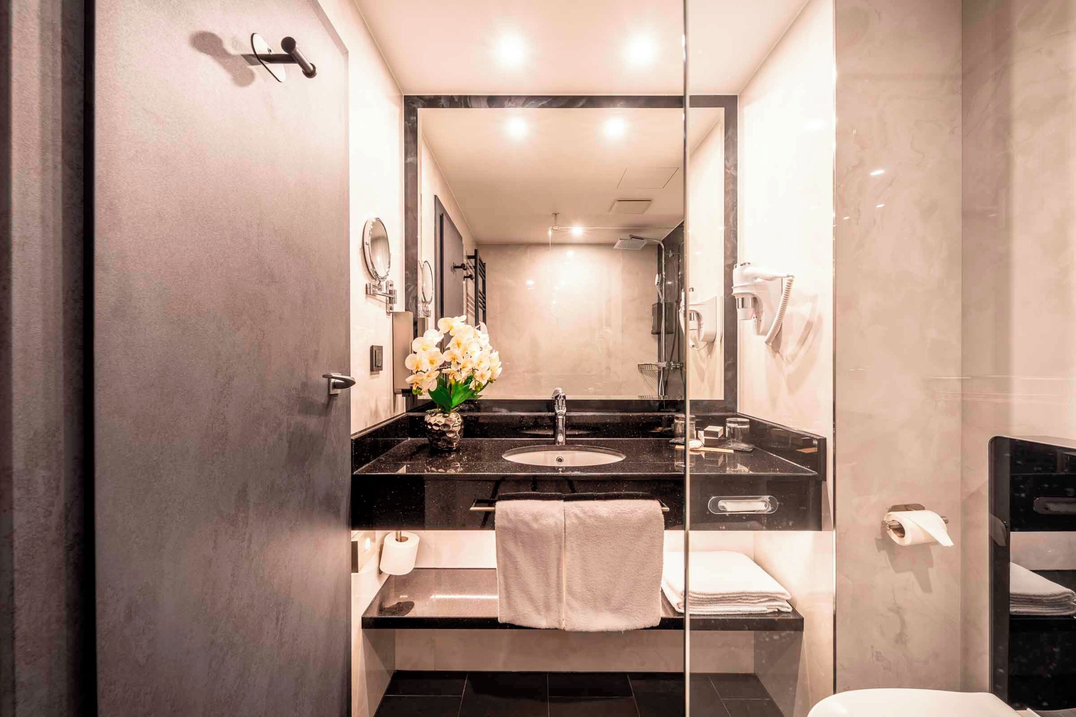 A modern bathroom with a black countertop, a sink, a mirror, and a glass-enclosed shower area.