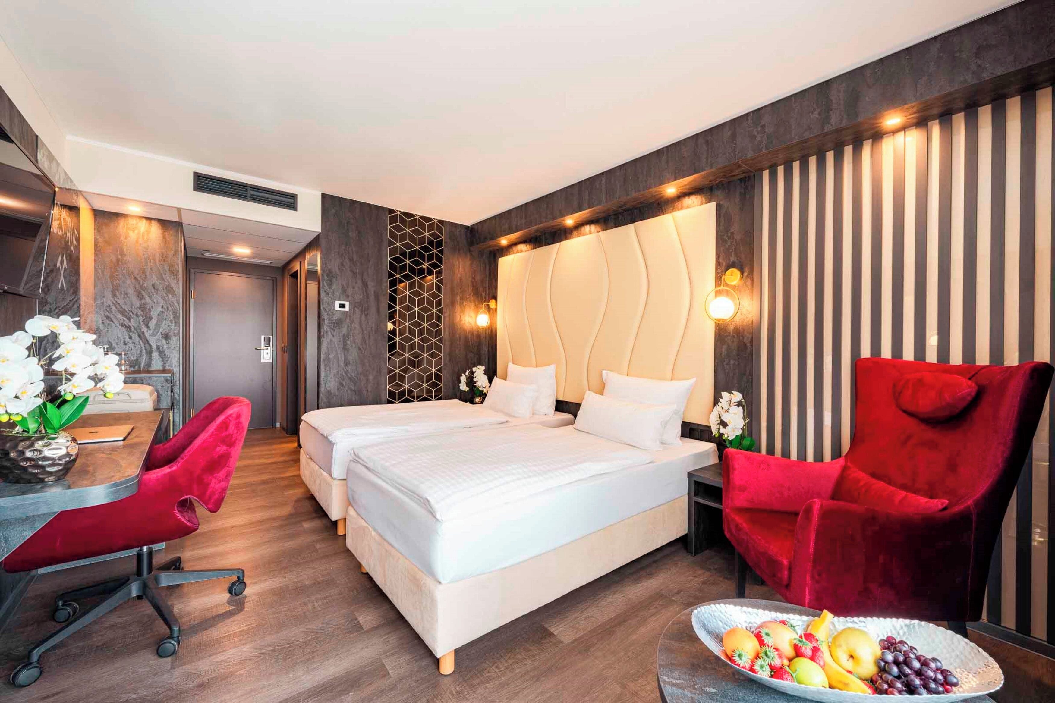 Habitación de hotel con una cama grande, un escritorio con silla, un sillón rojo y un frutero.