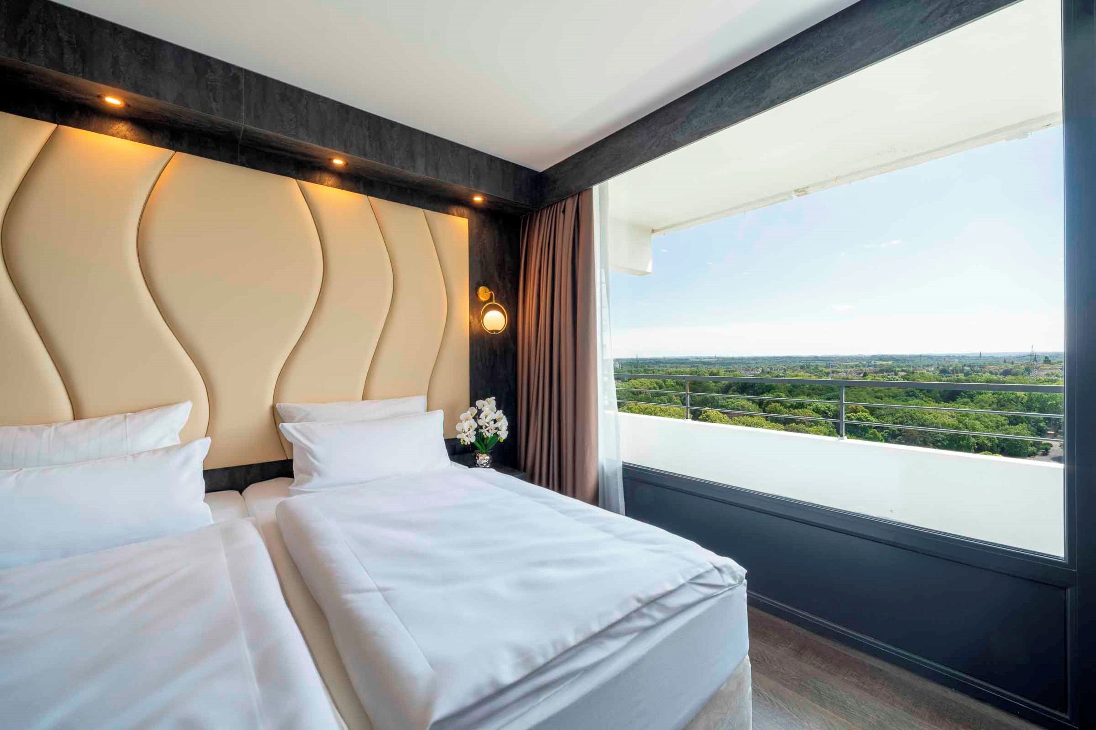 Ein Hotelzimmer mit einem großen Bett, Blick auf eine Stadtlandschaft und modernem Design.