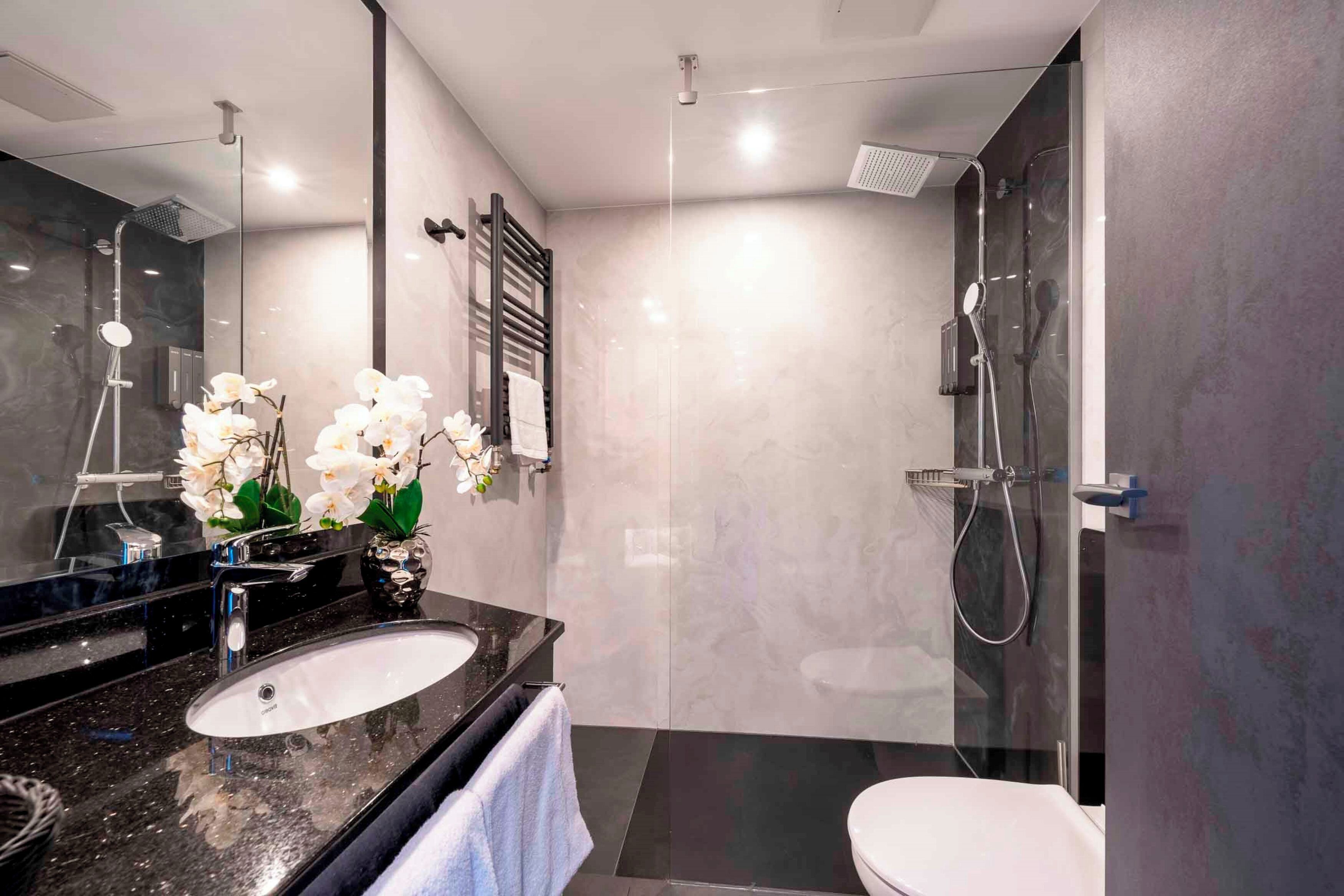 Un baño moderno con lavamanos de granito negro, inodoro blanco y zona de ducha con cerramiento de vidrio.