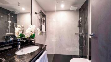 Un baño moderno con lavamanos de granito negro, inodoro blanco y zona de ducha con cerramiento de vidrio.