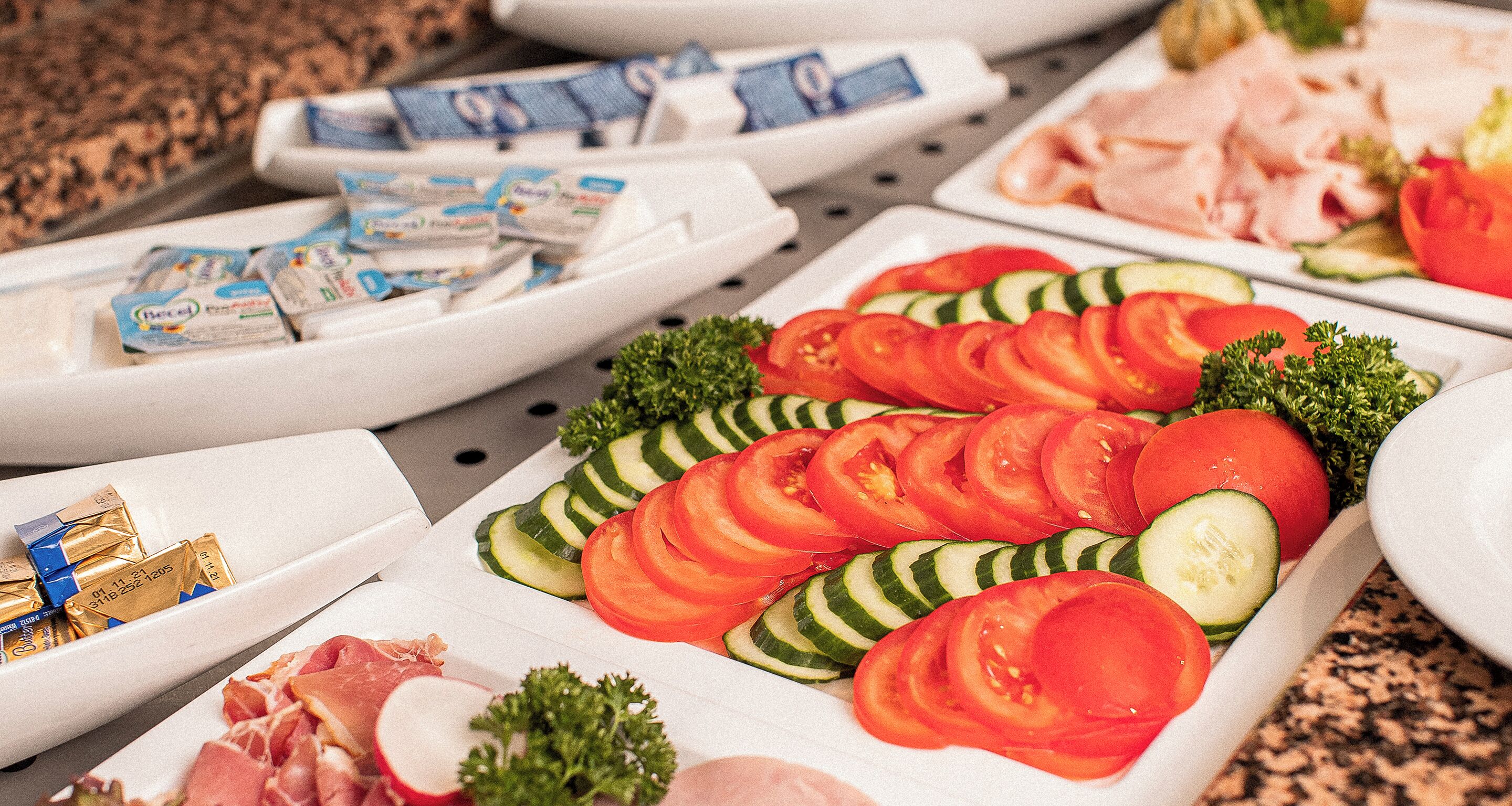 A buffet table with sliced tomatoes, cucumbers, and various meats.