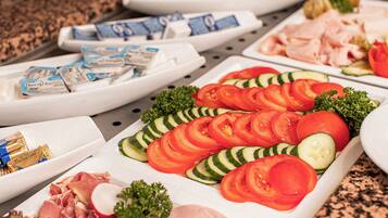 A buffet table with sliced tomatoes, cucumbers, and various meats.