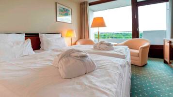A hotel room with two beds, a chair, a lamp, and a view of the outdoors.