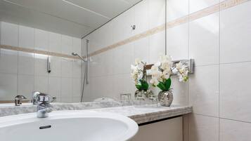 A bathroom with a white sink, a mirror, a shower, and decorative vases with orchids.