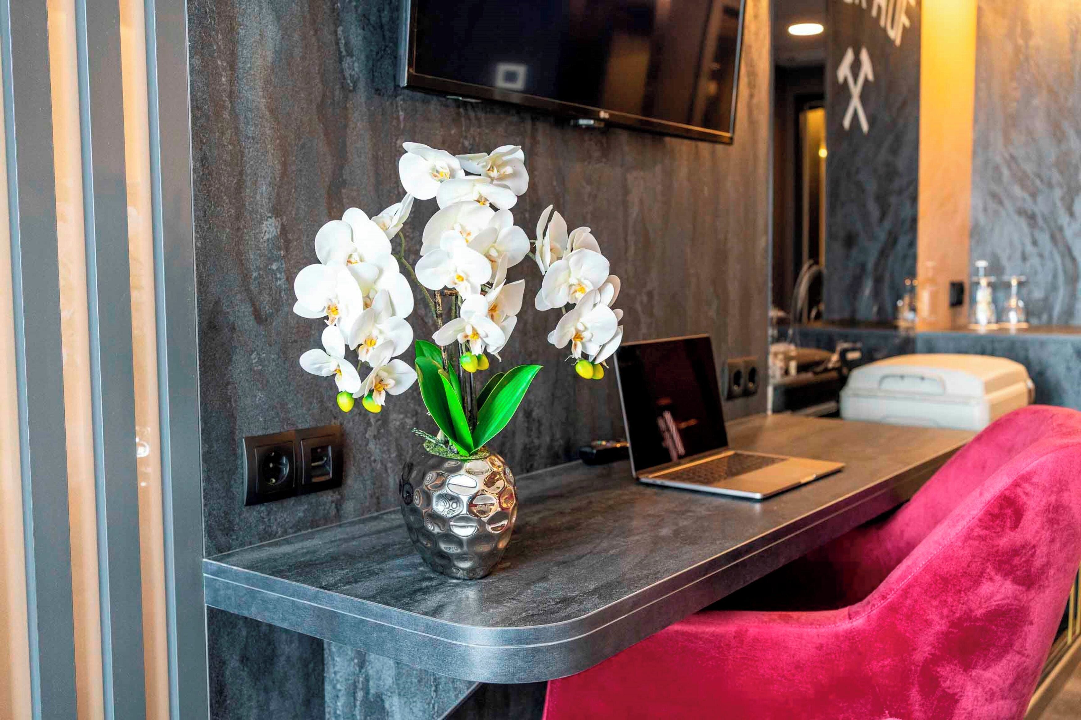 Un baño moderno con encimera de mármol, una computadora portátil y un jarrón con orquídeas blancas.