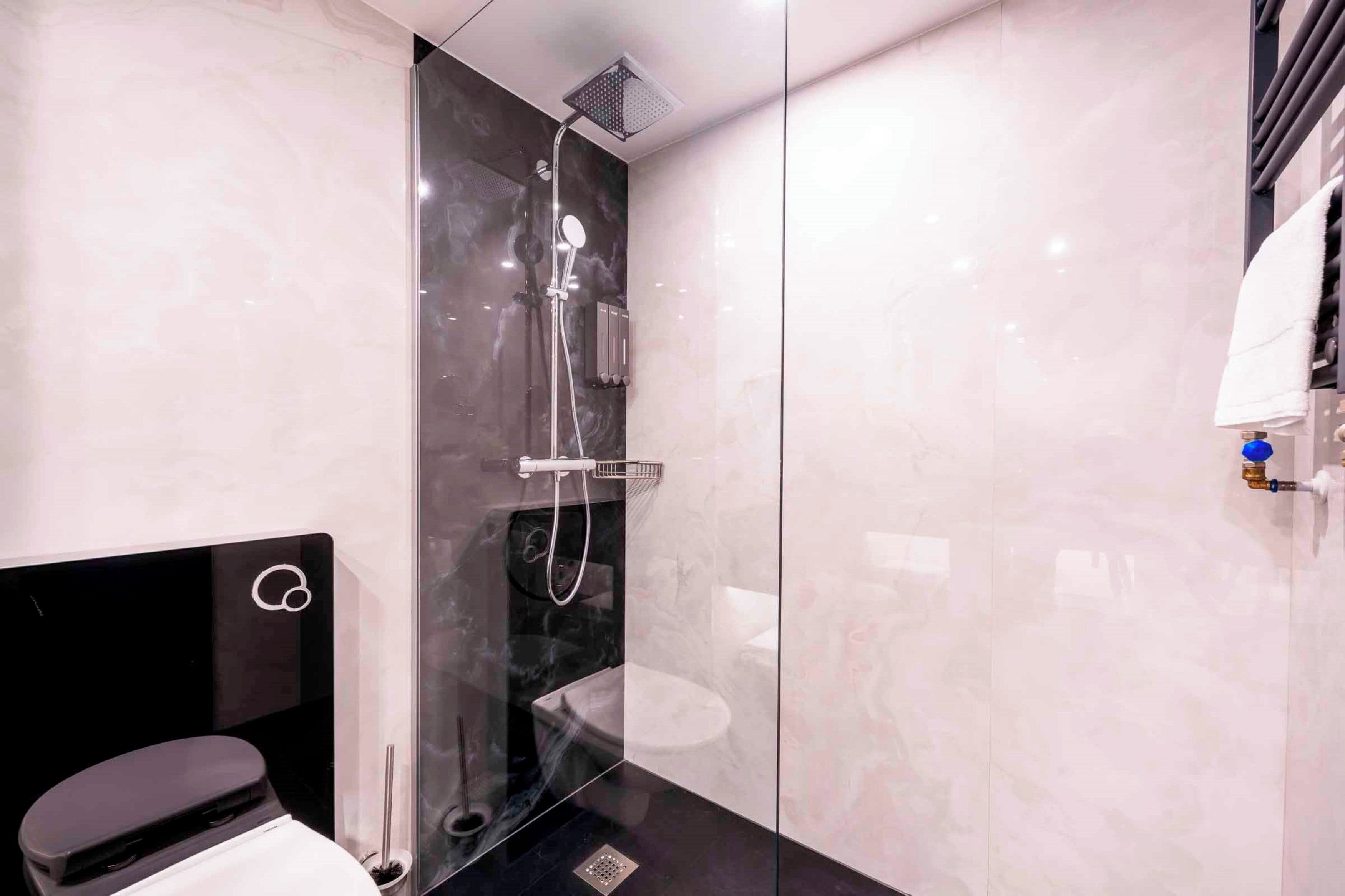 Un baño moderno con ducha envuelta en vidrio, tocador negro y inodoro blanco.