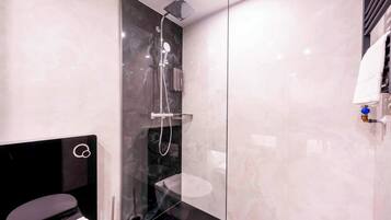 Un baño moderno con ducha envuelta en vidrio, tocador negro y inodoro blanco.