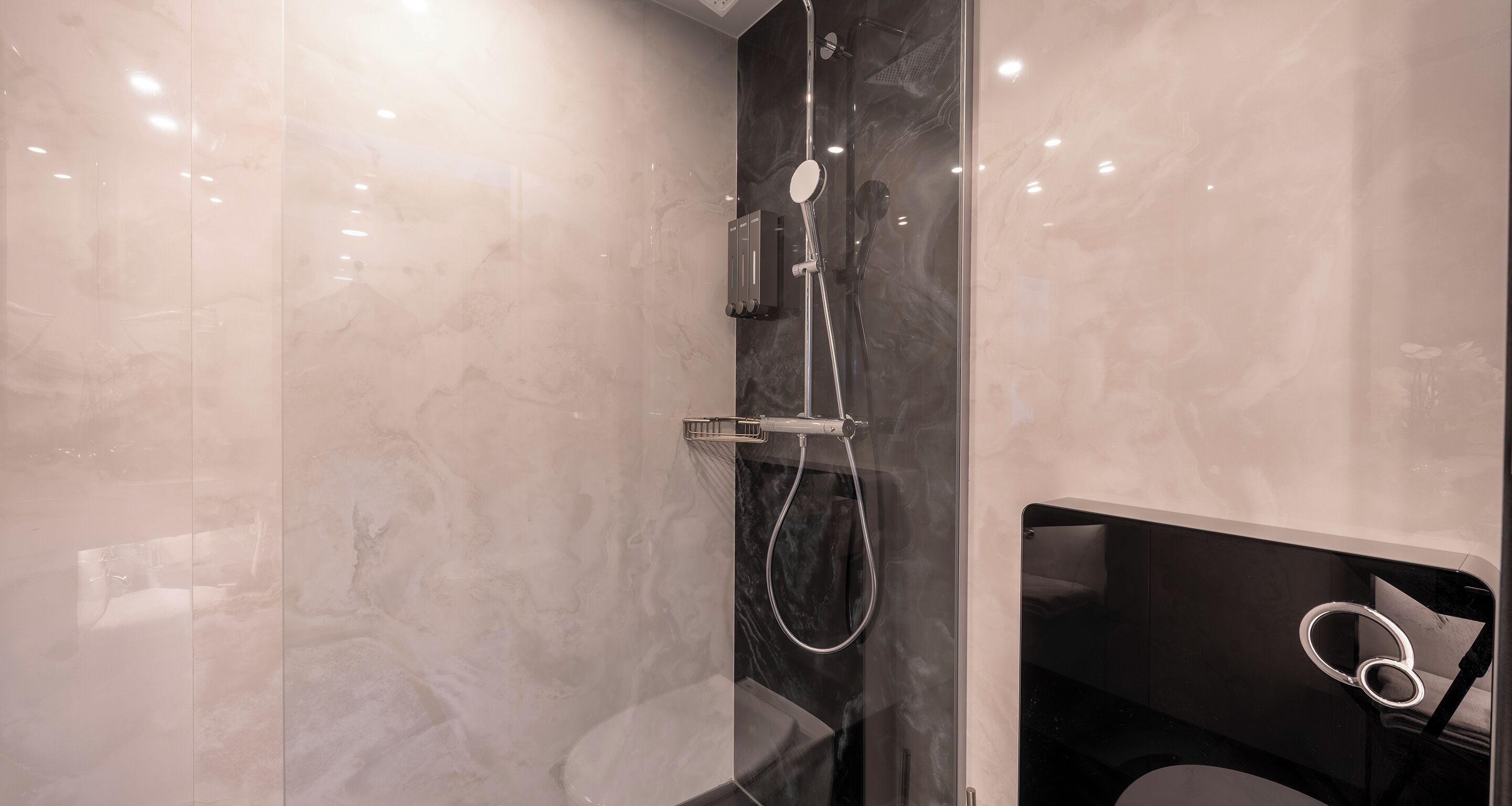 A modern bathroom with a glass-enclosed shower, marble walls, and a black vanity with a ring light.