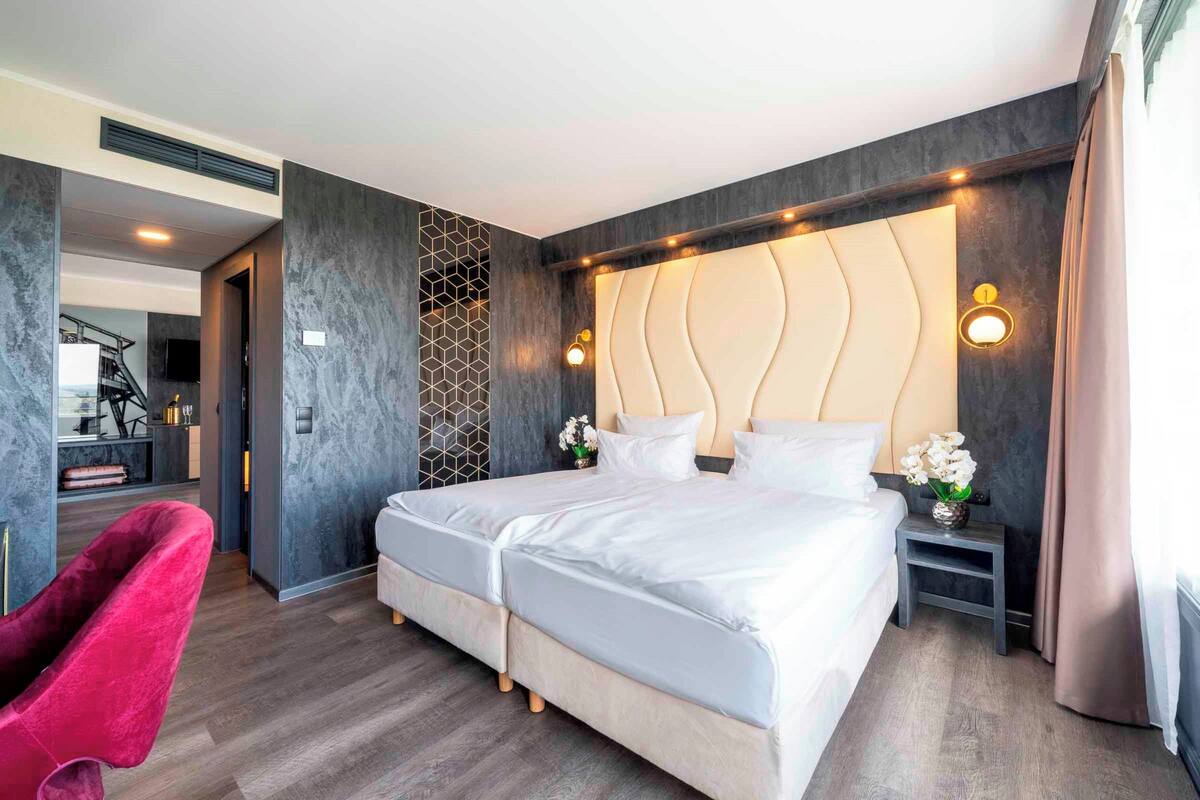 A modern hotel room with a large bed, a red chair, and a small table with a vase of flowers.