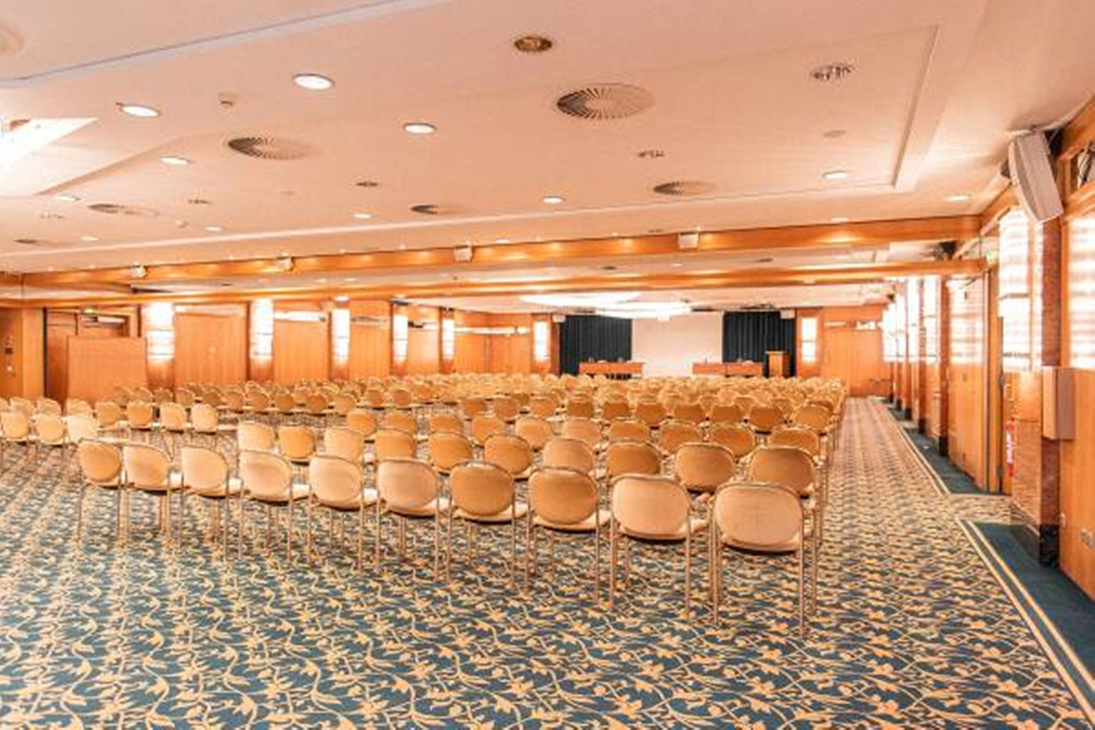 A large conference room with rows of chairs, a patterned carpet, and wooden paneling on the walls.
