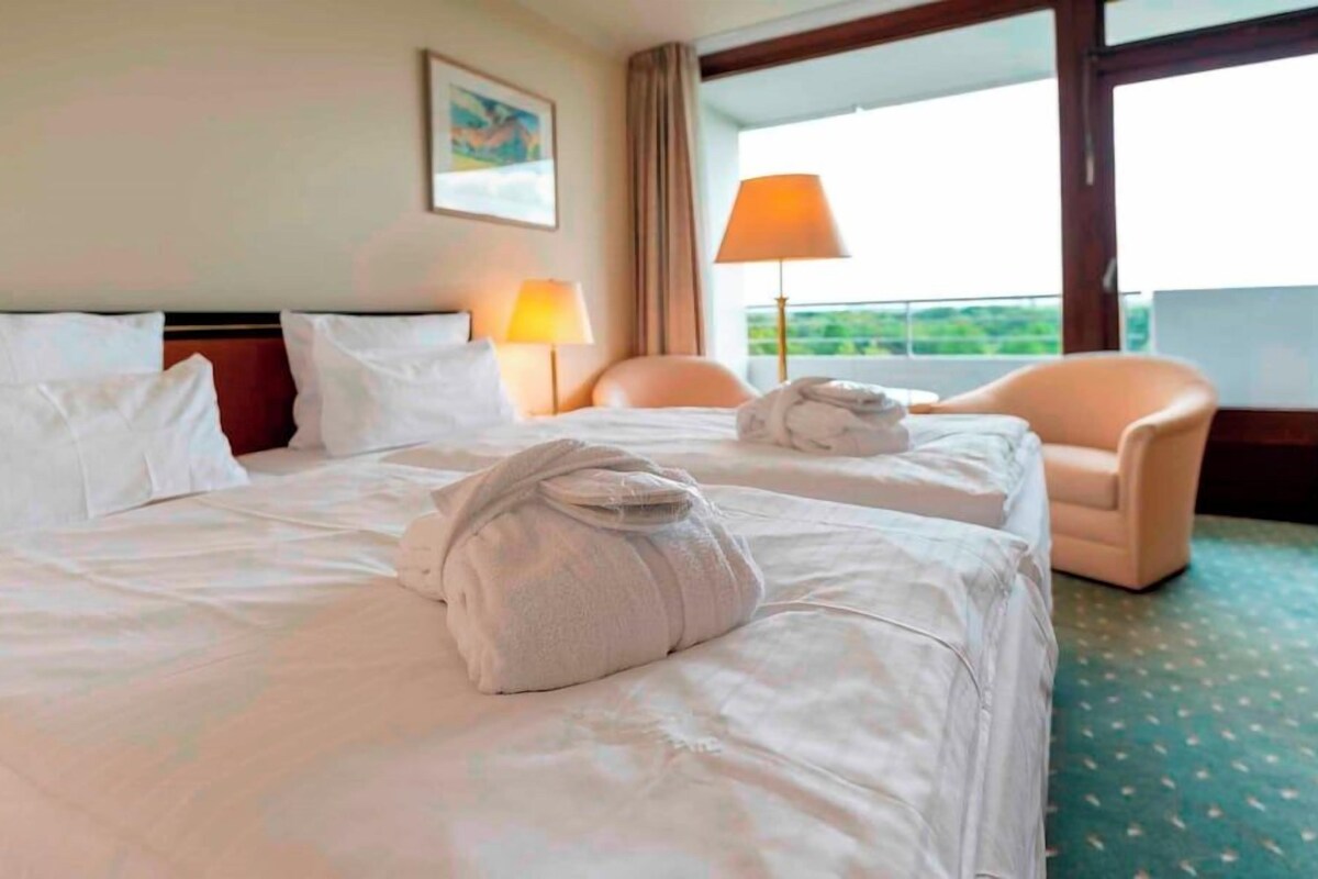 Habitación de hotel con dos camas, una silla, una lámpara y vistas a zonas verdes.