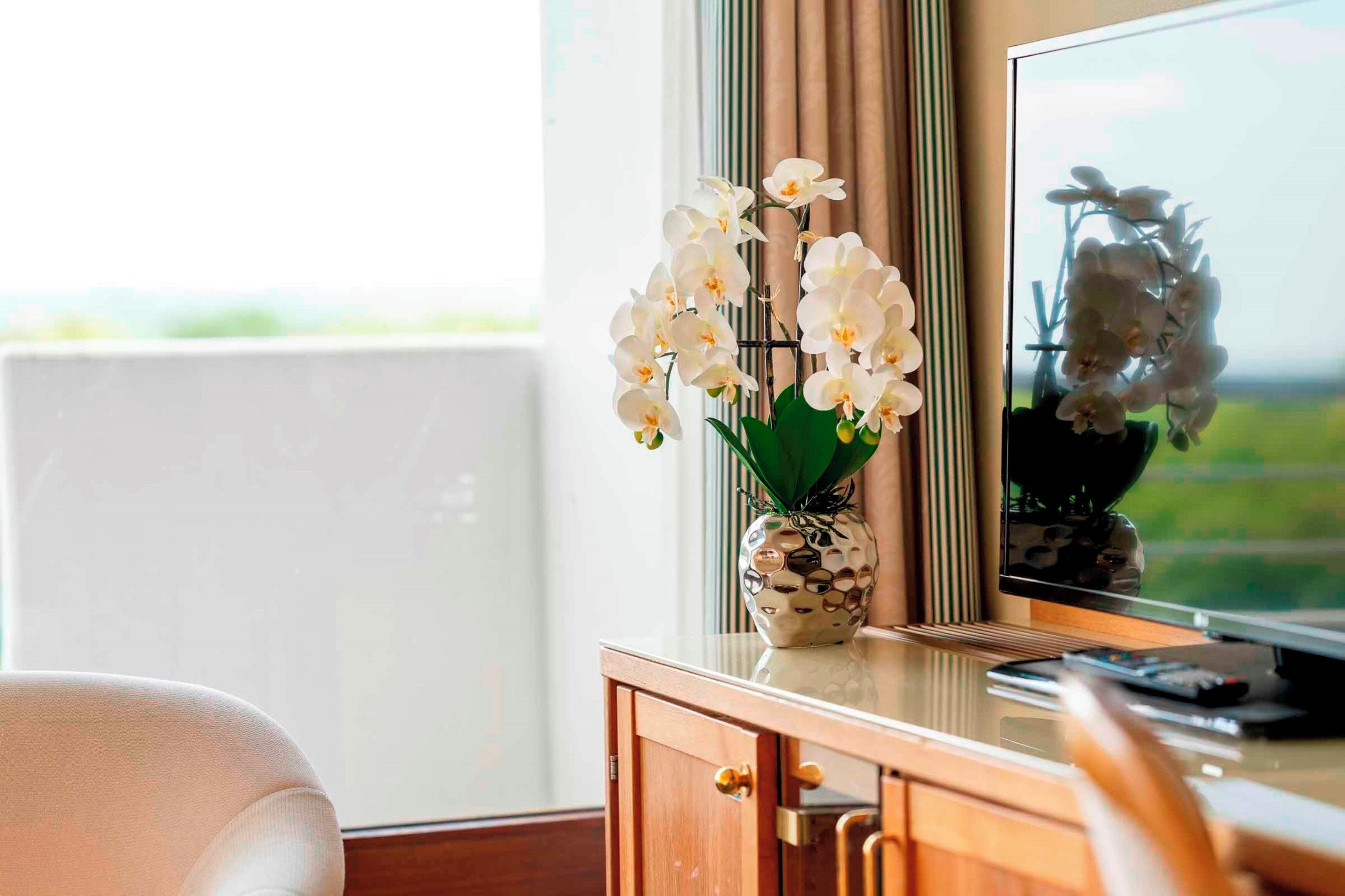 Une pièce dotée d’une grande fenêtre, d’une armoire en bois et d’un vase contenant des orchidées blanches.
