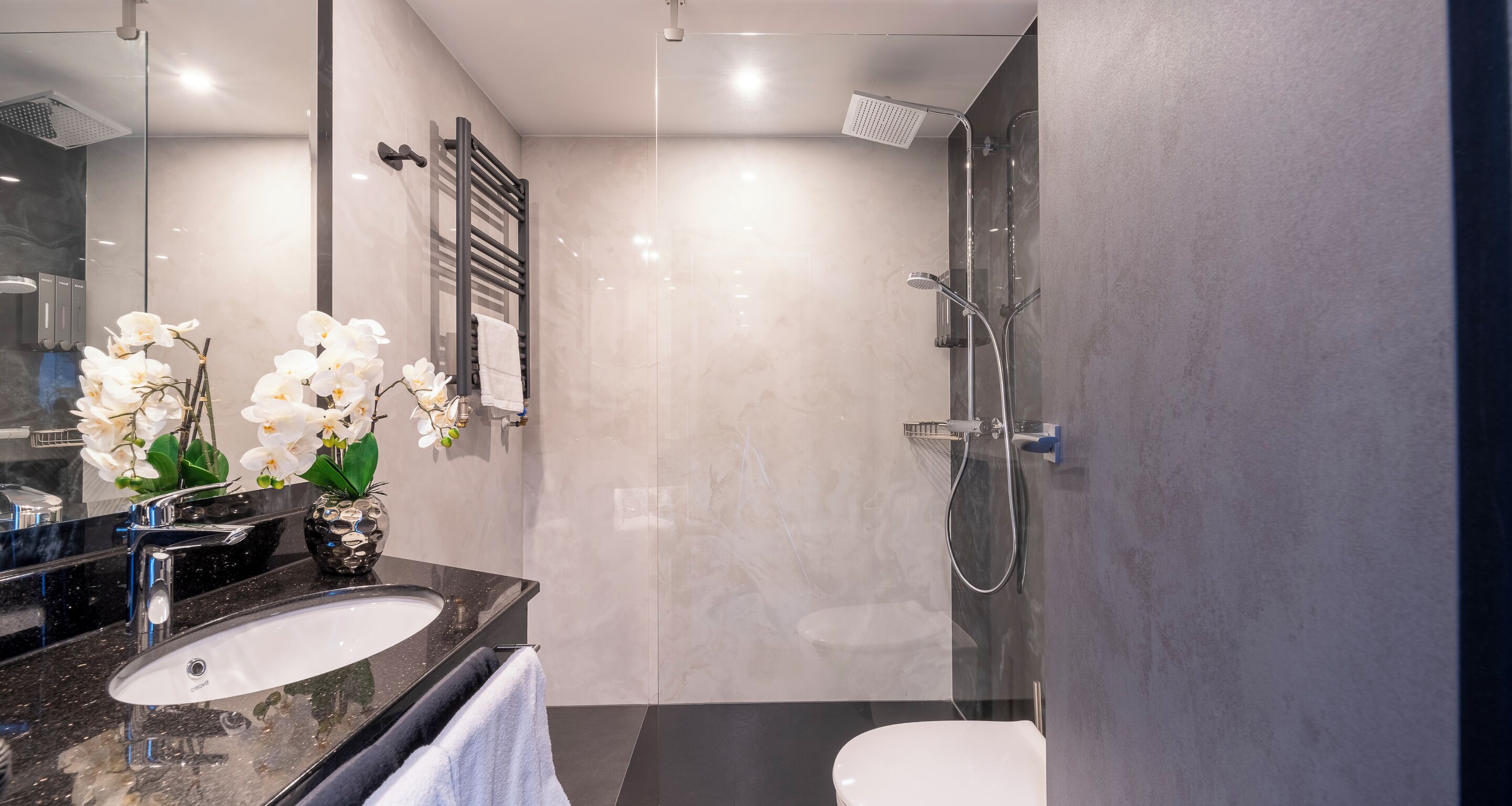 Ein modernes Badezimmer mit einem schwarzen Granittischwaschbecken, einer weißen Toilette und einer Duschkabine aus Glas.