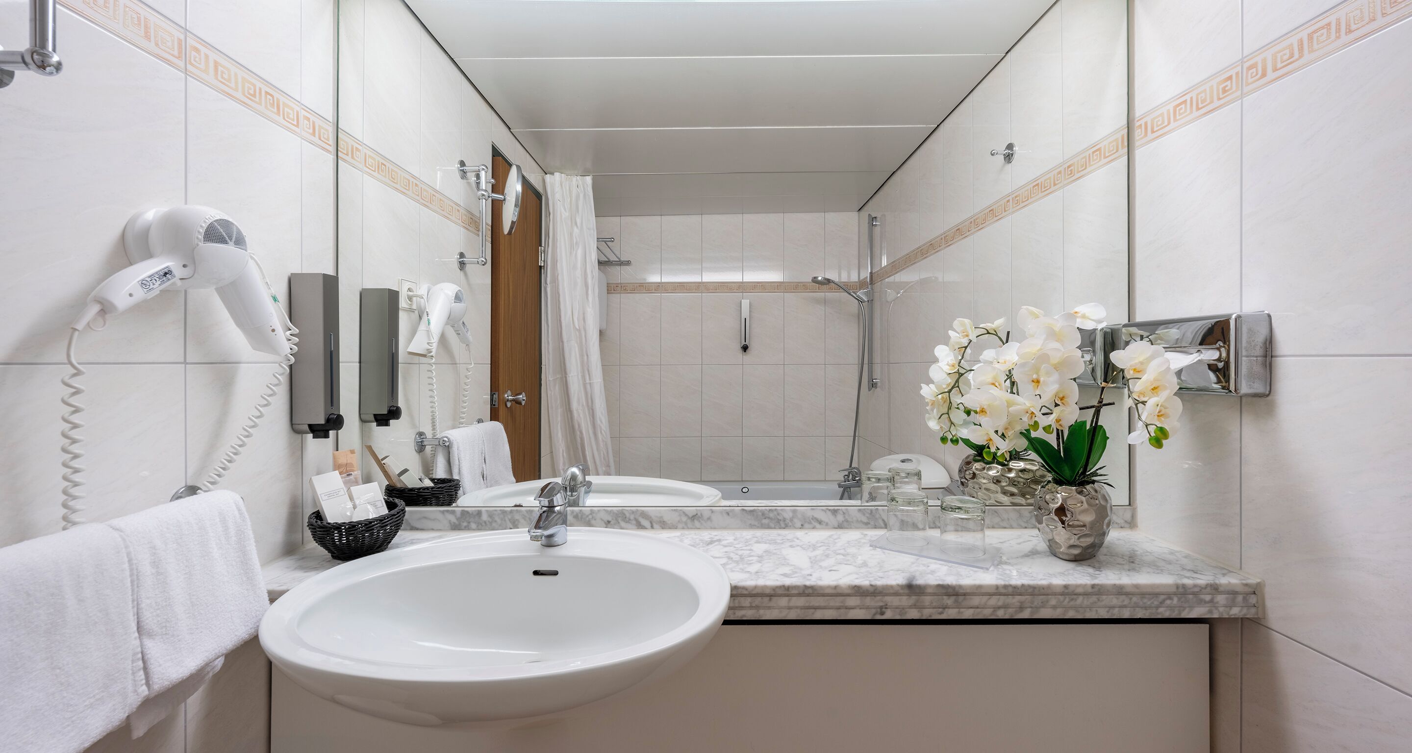 Une salle de bain équipée d’un lavabo, d’un miroir, d’un sèche-cheveux et d’un espace douche.