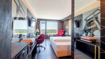 A modern hotel room with a bed, desk, chair, and a large window offering a city view.