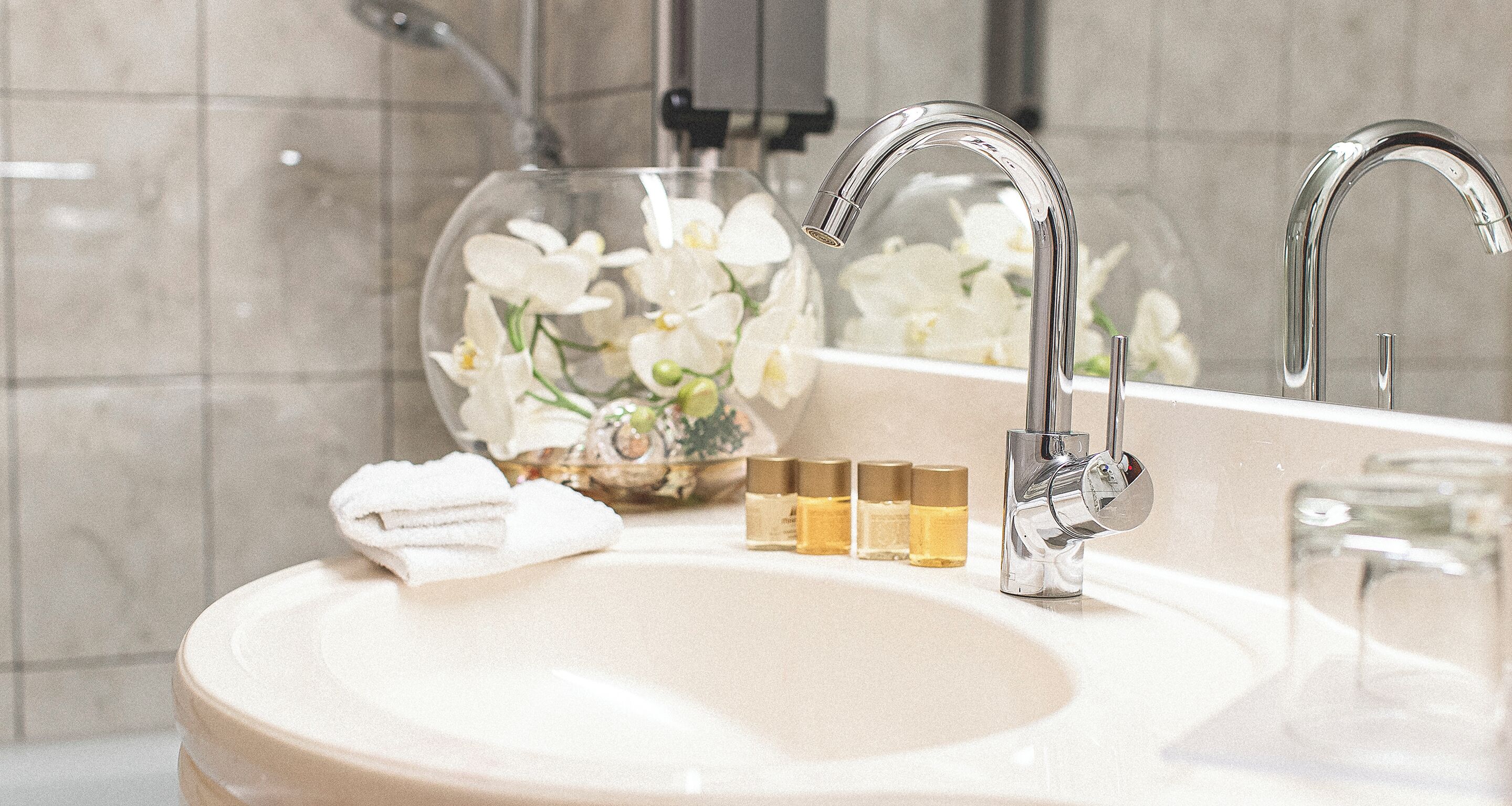 A bathroom sink with a glass vase of white flowers, a towel, and three small bottles.
