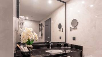 A modern bathroom with a black marble sink, a large mirror, and white orchids.