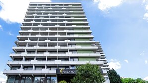 Ein modernes, mehrgeschossiges Gebäude mit flacher Fassade, Balkonen und einem sichtbaren Schild für 'Plaza Hotel'.